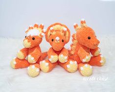 three orange stuffed animals sitting on top of a white fur covered floor next to each other