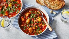 two bowls of stew with bread and water on the side, next to each other