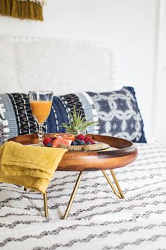 a tray with fruit and juice on it sitting on a bed next to pillows,