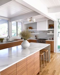 a large kitchen with white counter tops and wooden cabinets in the center, along with two stools