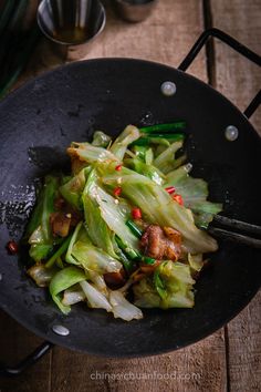 a wok filled with stir fry vegetables on top of a wooden table next to utensils