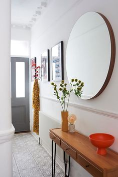 there is a vase with flowers on the table in front of the mirror and an orange bowl next to it