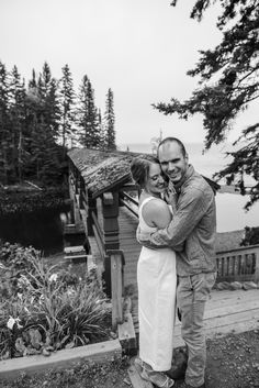 a man and woman standing next to each other in front of a house with trees