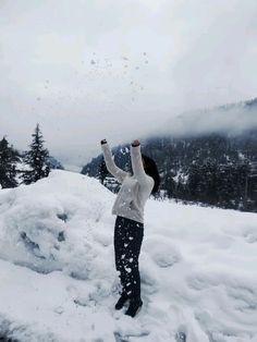 a woman standing on top of a snow covered slope with her arms in the air