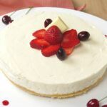 a cheesecake with strawberries and cherries sits on a white plate, ready to be eaten