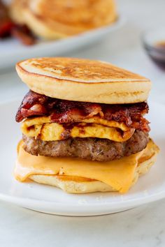 a bacon, egg and cheese breakfast sandwich on a plate with pancakes in the background