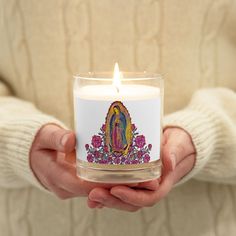 a person holding a lit candle in their hands with the image of jesus on it