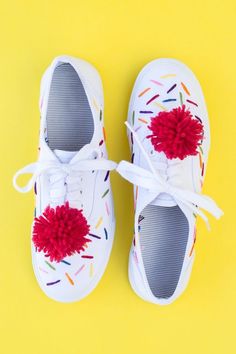 a pair of white shoes with red pom - poms on the laces