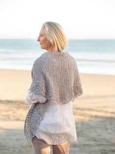 a woman standing on top of a sandy beach next to the ocean wearing a sweater