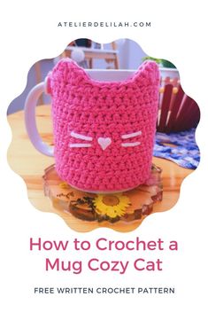 a pink crochet mug cozy cat sitting on top of a wooden table