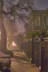 an empty sidewalk in the middle of a residential area at night with street lights on