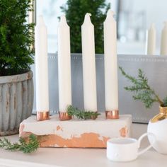 four candles are sitting on top of a table next to a potted plant and cup