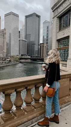 a woman standing on the side of a bridge next to a river with buildings in the background