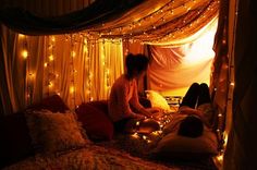 a woman sitting on top of a bed under a canopy covered in fairy string lights