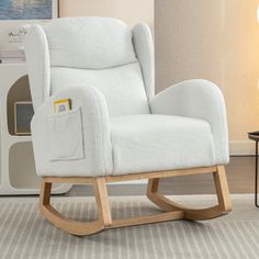 a white rocking chair in a living room next to a table with a lamp on it