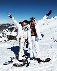 two snowboarders pose for a photo on the top of a mountain with their arms in the air