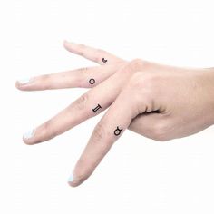 a person's hand with two fingers and one finger has three small tattoos on it