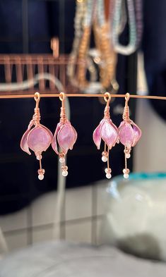 three pink earrings hanging from a wire in front of a glass vase with flowers on it