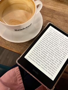 a tablet sitting on top of a wooden table next to a cup of coffee and saucer