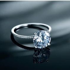 a white diamond ring sitting on top of a black surface with the reflection of it