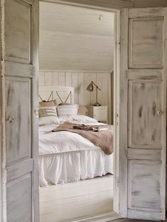 an open door leading to a bed in a room with white walls and wooden floors