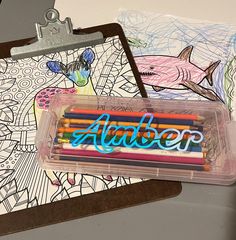 an assortment of colored pencils in a plastic container on top of a drawing pad