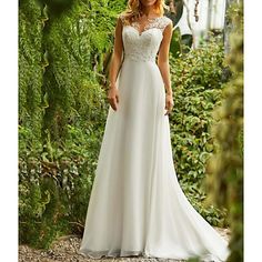 a woman in a white wedding dress standing on a path surrounded by plants and flowers