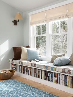 a window seat with bookshelves in front of it and a blue rug on the floor