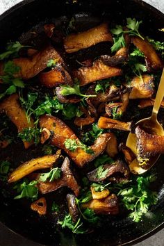 a skillet filled with chicken and greens on top of a table next to a spoon