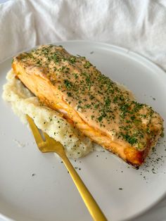 a piece of salmon and mashed potatoes on a white plate with a yellow fork