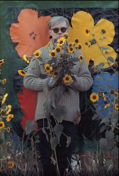 an older woman holding flowers in front of a colorful wall with sunflowers on it