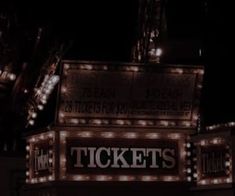 a lighted ticket booth sign at night with lights on it's sides and the words tickets written in large letters