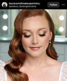 a woman with red hair and makeup looks down at her cell phone while wearing a white dress