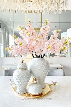 a vase with pink flowers in it sitting on a table next to a mirror and chandelier