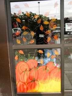 a store front window with pumpkins and leaves painted on the glass in different colors