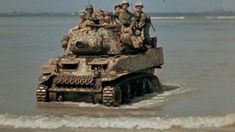 a group of soldiers riding on top of a tank in the water at the beach