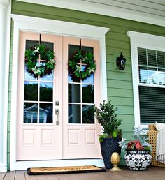 two wreaths on the front door of a house with potted plants in front