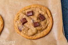 two chocolate chip cookies sitting on top of a piece of wax paper next to each other