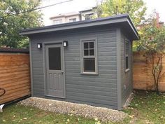 a small gray shed sitting in the middle of a yard next to a wooden fence