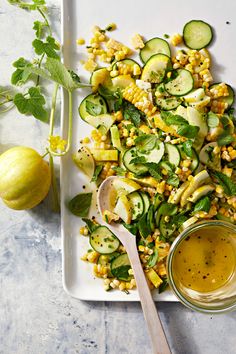 a white plate topped with zucchini and corn next to a bowl of dressing