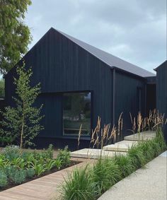 two black buildings with wooden walkways next to them and plants in the foreground