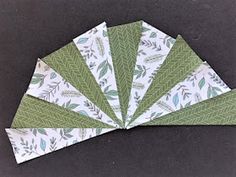 six green and white paper napkins with leaves on them, sitting on a black surface