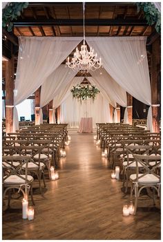 the inside of a wedding venue with white drapes, candles and chandeliers