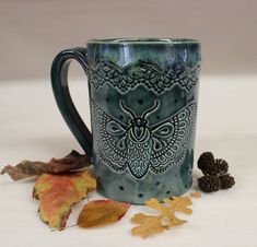 a blue coffee mug sitting on top of a table next to leaves and acorns