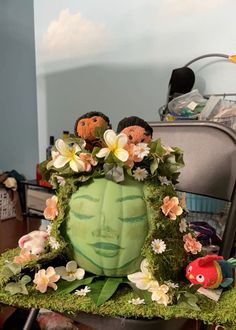 an arrangement of fake flowers and plants in a green pumpkin shaped planter on a chair