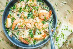 a bowl filled with shrimp and parsley on top of a wooden table next to bread