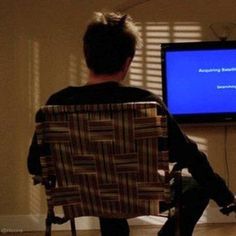 a person sitting in a chair watching something on the television screen while holding a remote control