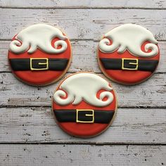 three decorated cookies sitting on top of a wooden table with white frosting and red icing