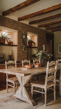 a dining room table and chairs in front of a brick wall with potted plants