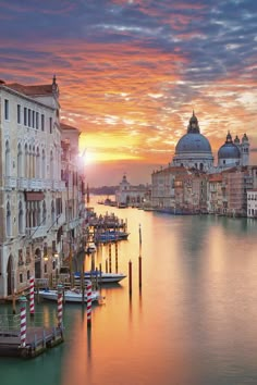 the sun is setting in venice, italy as boats are docked on the water and buildings line the shore